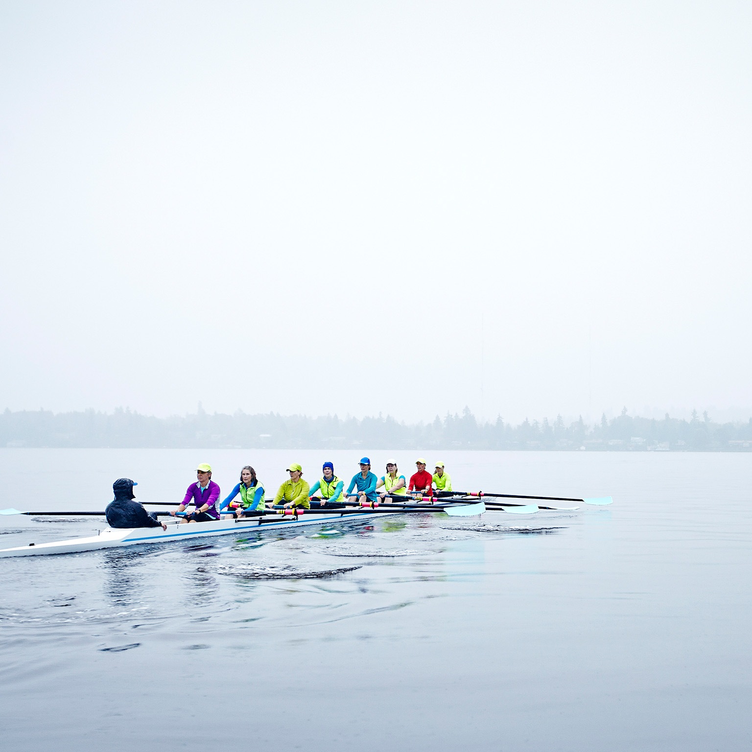 Group of mature female rowers rowing eight person boat during rainy morning practice