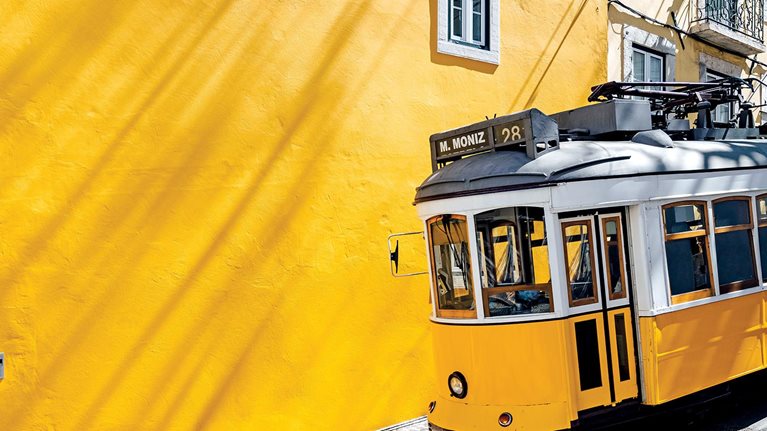 Yellow tram moving past yellow building in Lisbon, Portugal