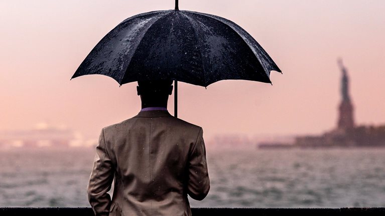 Rear view of man with umbrella standing by railing against sea.
