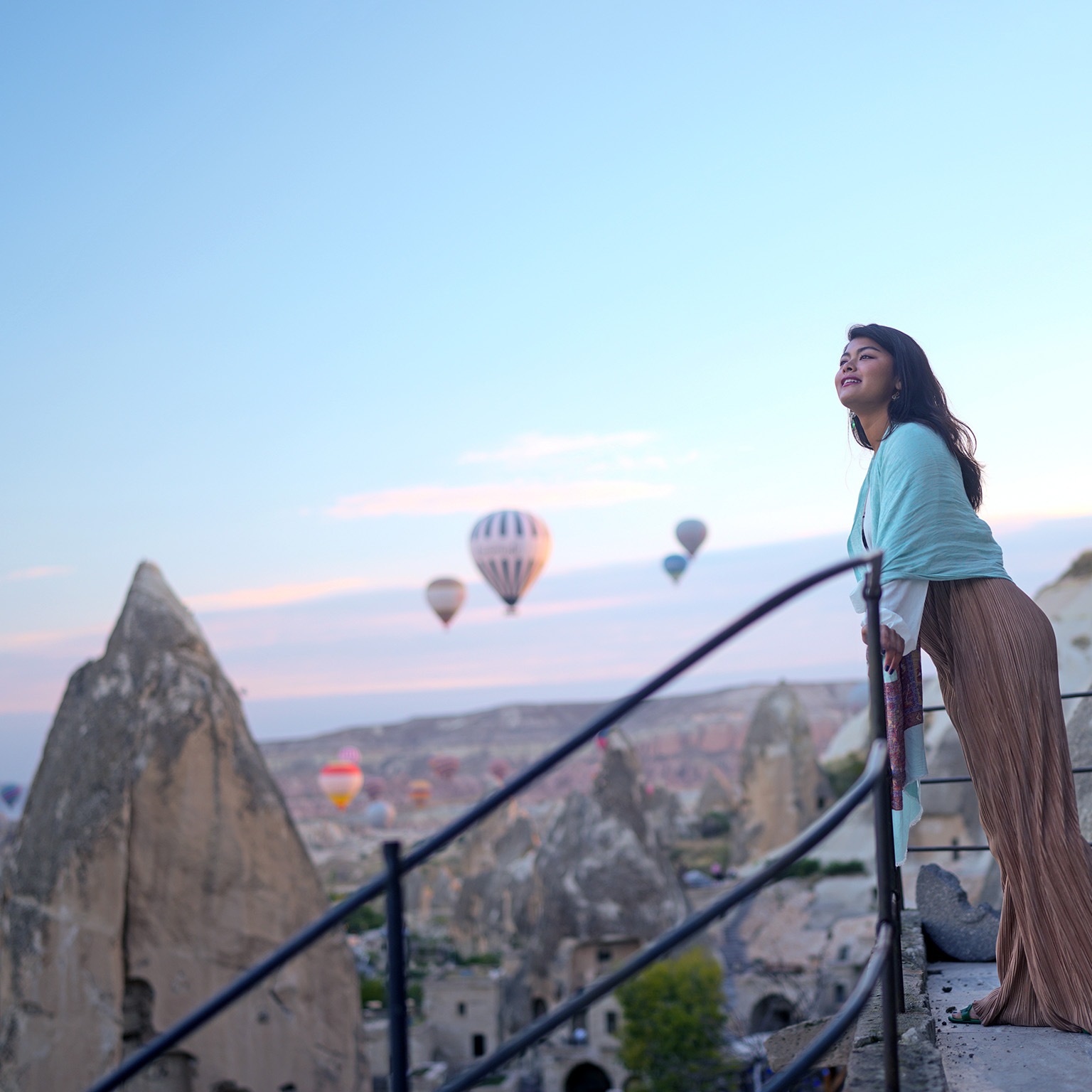Portrait of young female tourist watching hot air balloons from a balcony on a cliff