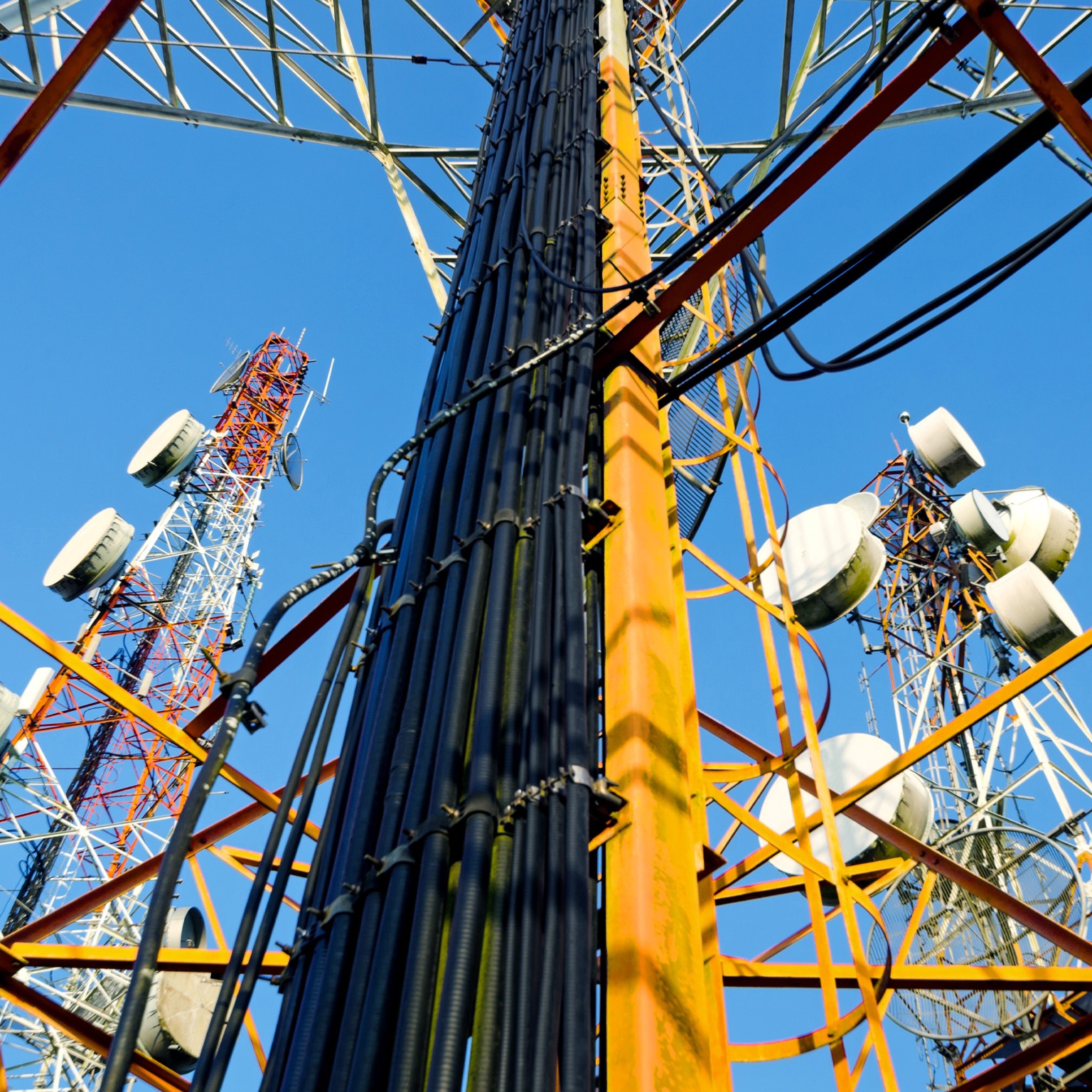 A low-angle view of a complex of telecommunication towers against a clear blue sky. 
