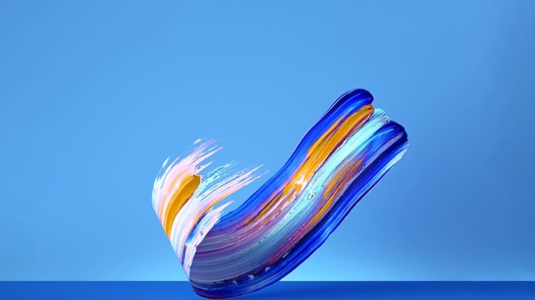 Against a vivid blue background, a vibrant, multicolor brushstroke of paint gracefully curves upwards.