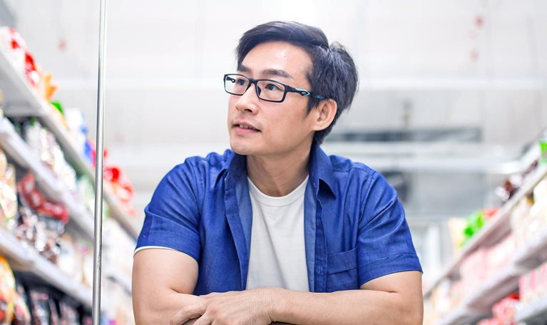 An Asia mature man pushes shopping cart and browses for products in groceries shop