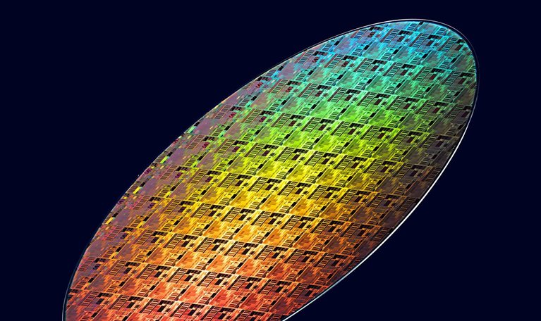 Colorful iridescent semiconductor wafer with intricate microchip patterns displayed against a dark background.