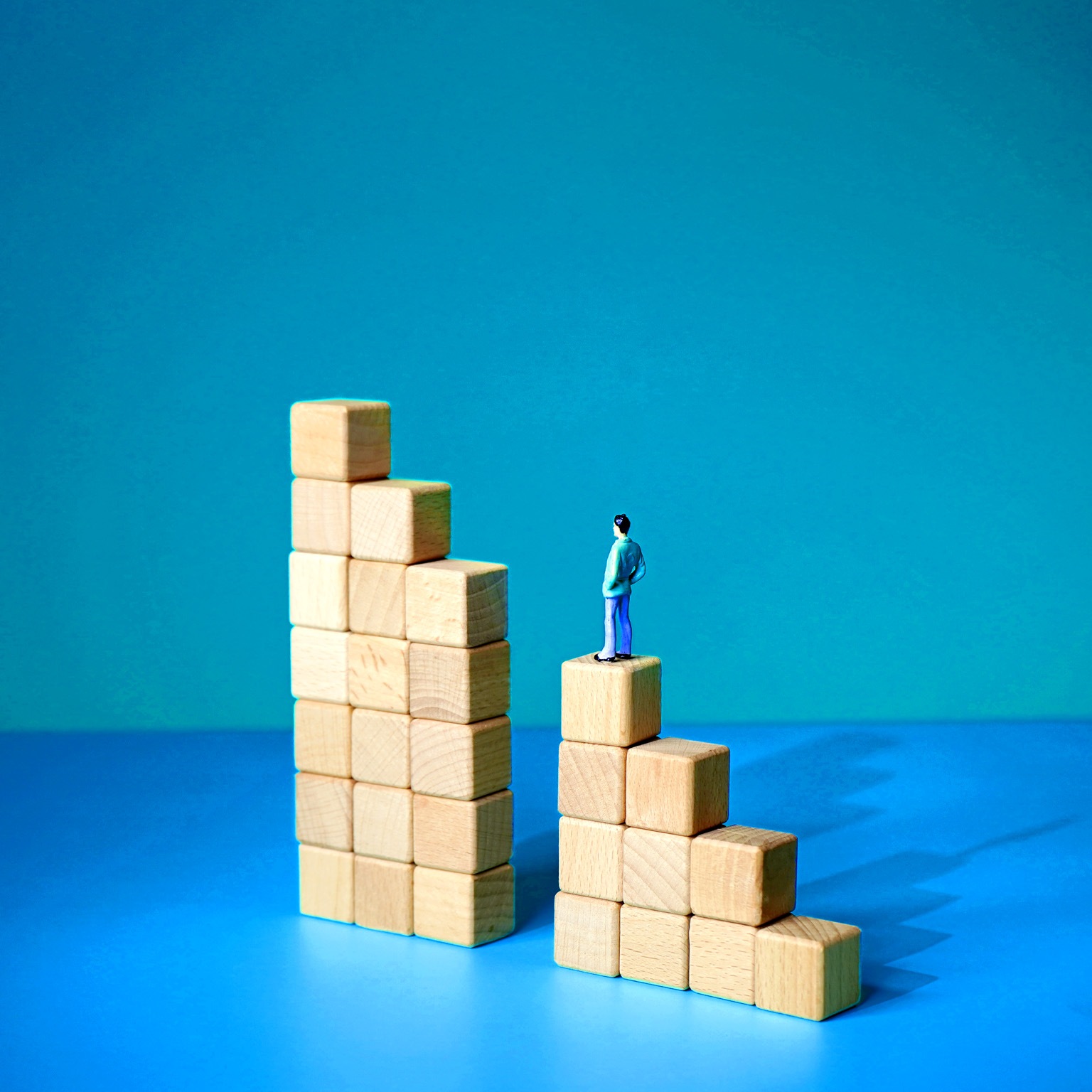 A series of wooden blocks arranged in a stair-like formation, with a gap in the middle where a vertical set of blocks is missing. A tiny man stands, unable to continue forward with his arms hanging at his sides.