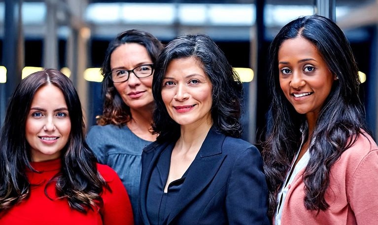 A diverse group of four professional women look confidently forward.