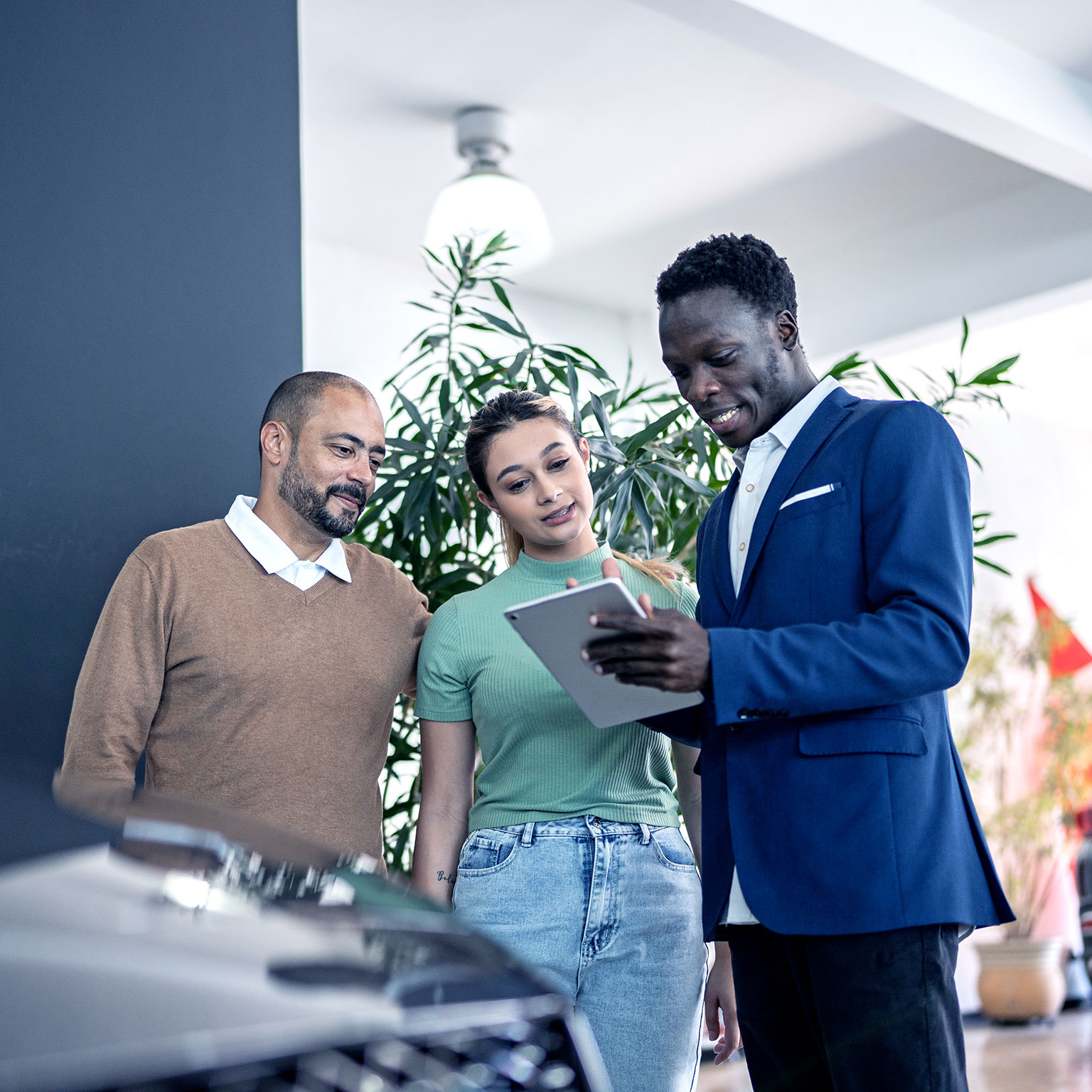 Car salesman using digital tablet talking about new car to customers in a store