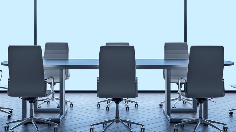 A modern boardroom table and chairs with large windowpanes behind it.