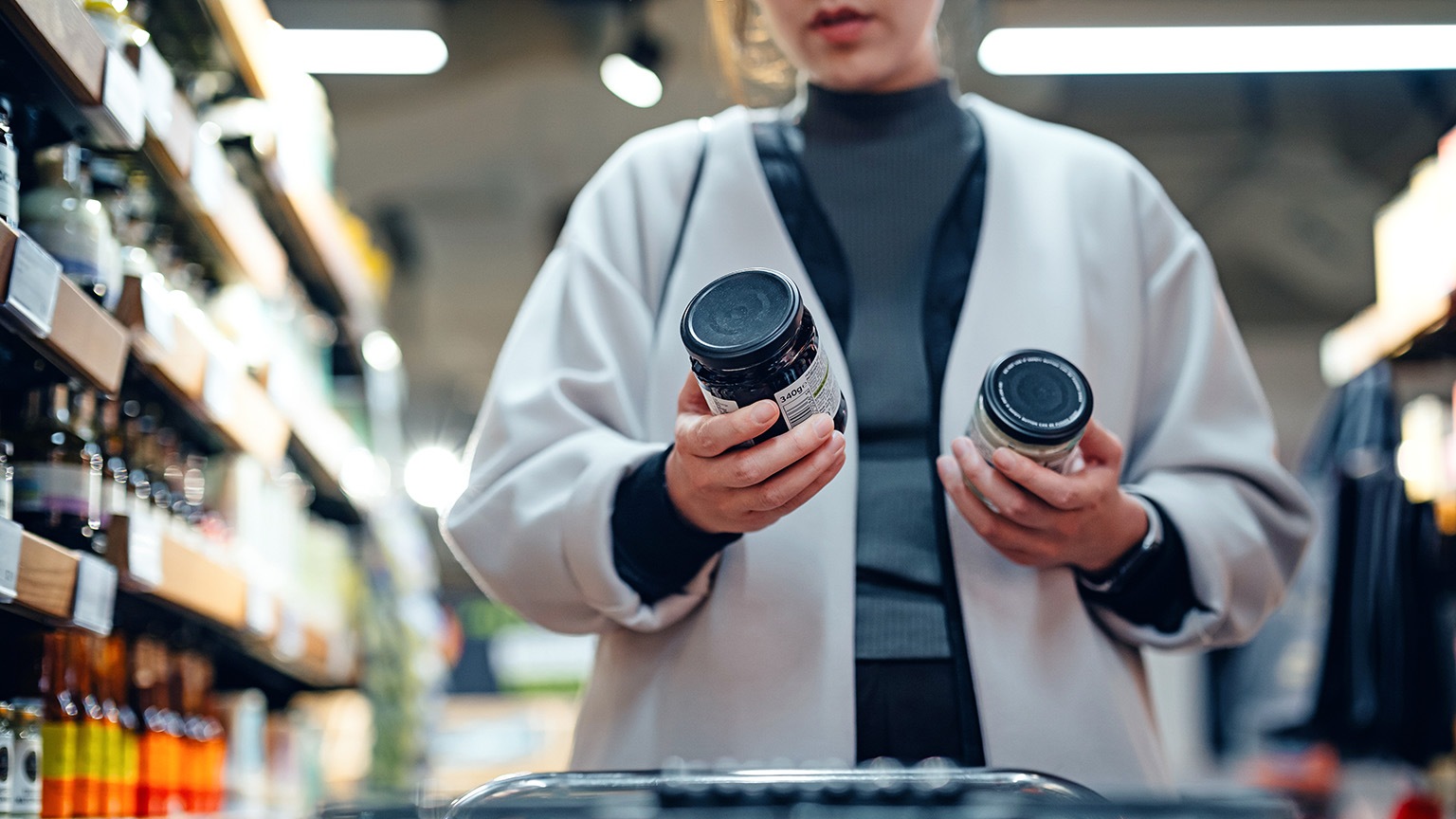 A close up shot of a woman comparing the labels of two different cooking sauce brands.