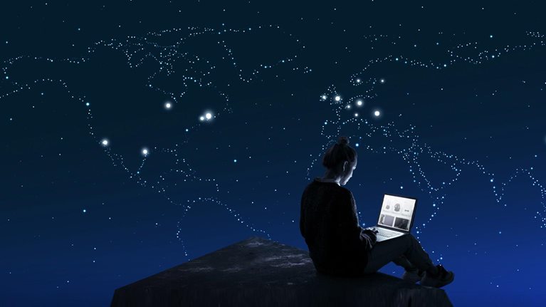 Woman sitting on rock with laptop, night sky making constellation of globe in the stars
