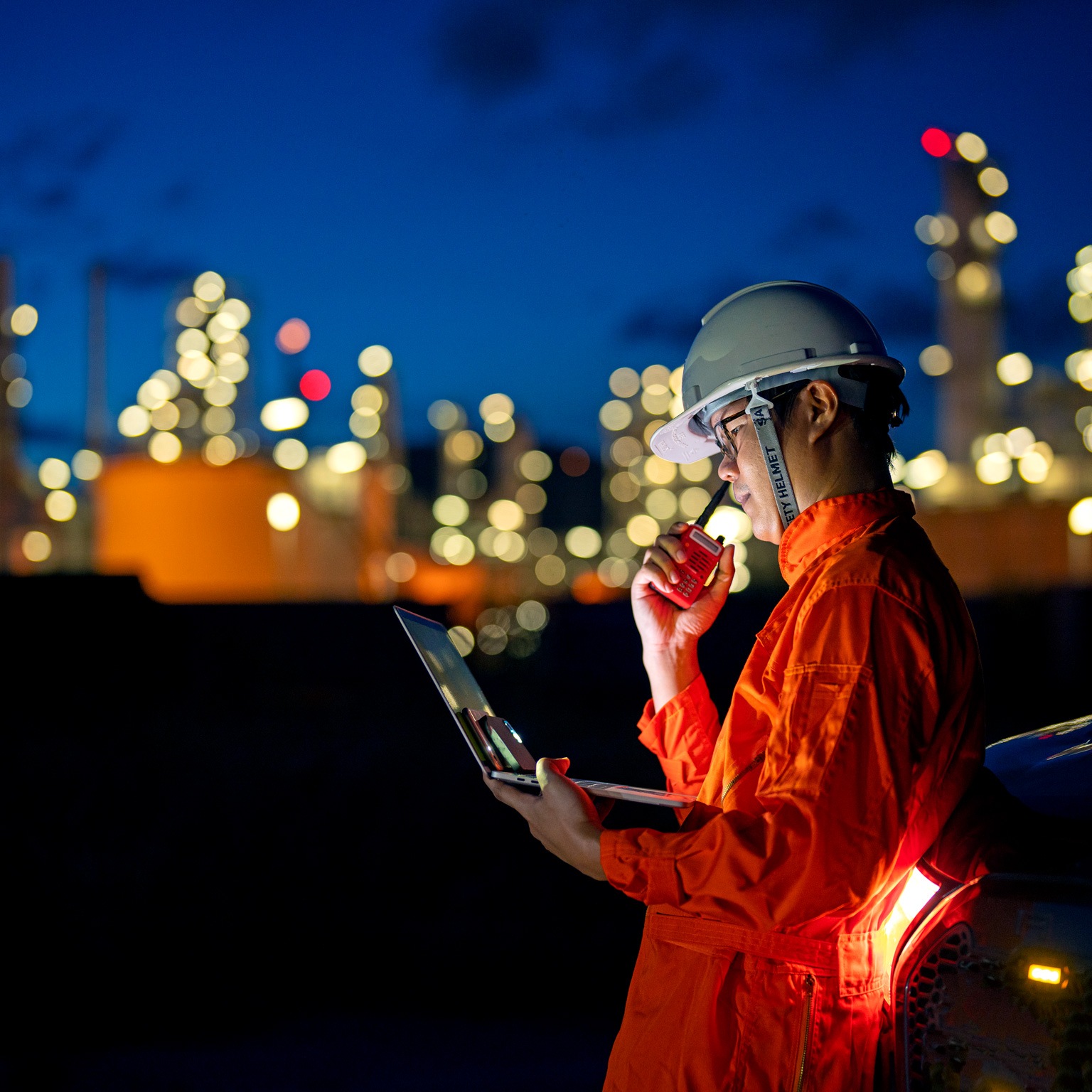 Industrial worker in overalls, helmet holding digital equipment such as laptop, walkie talkie, digital lamp