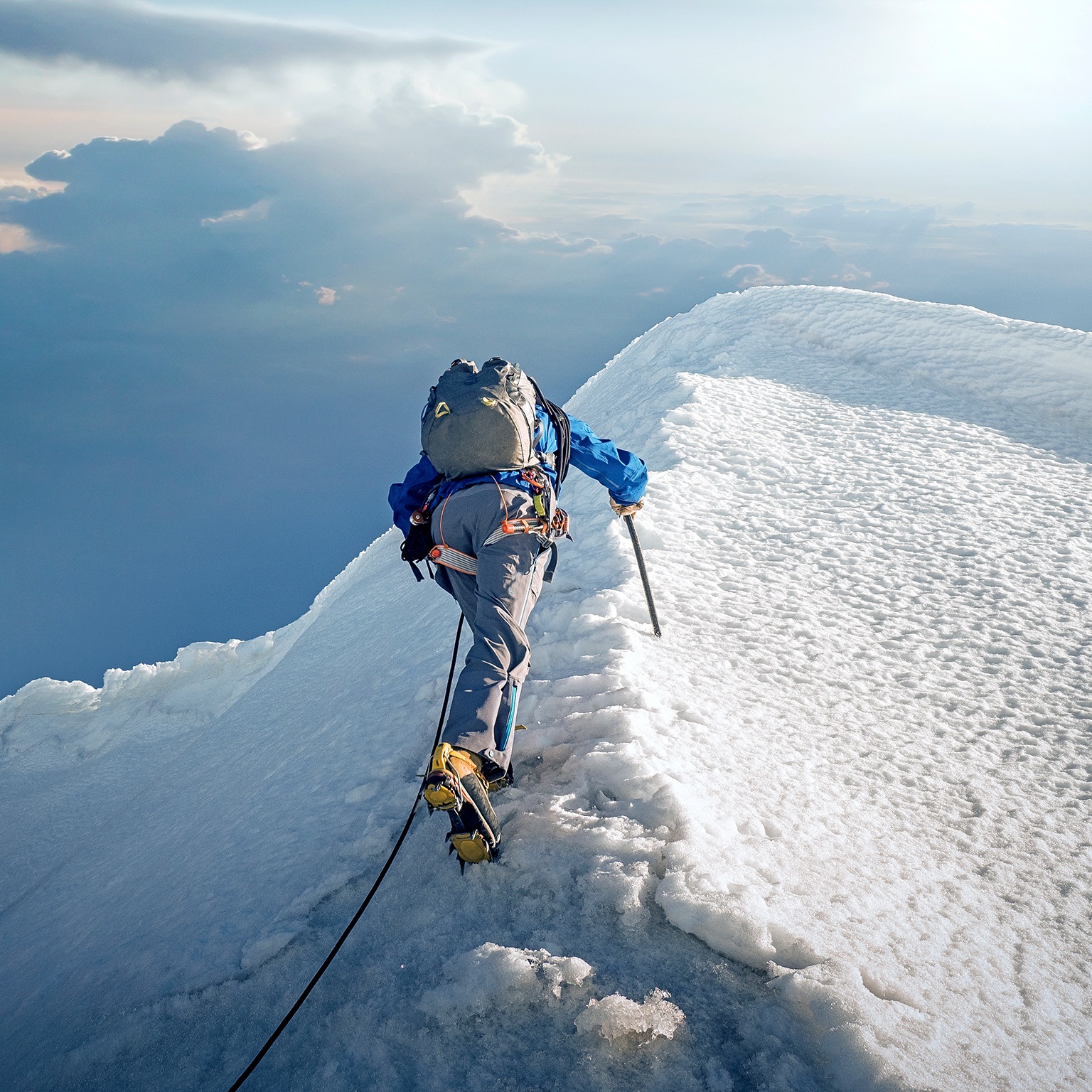 A lone climber ascending a snowy ridge in the Alps