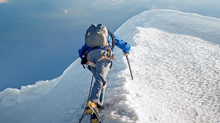 A lone climber ascending a snowy ridge in the Alps