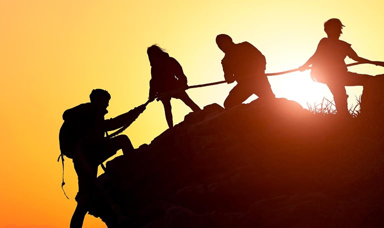 Silhouette of the climbing team helping each other while climbing up in a sunset