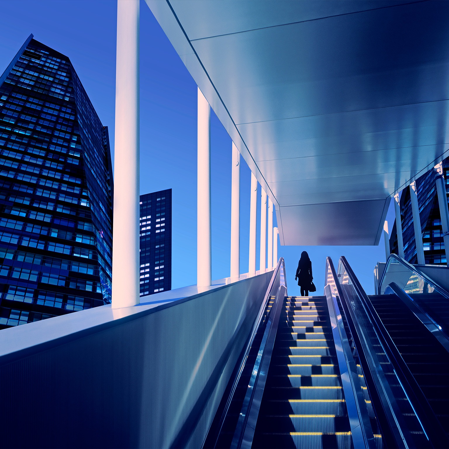 Early evening at modern business district with silhouette of businesswoman on top of a moving escalator.