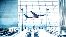 View from the inside of a modern bright airport with an airplane taking off outside the window.