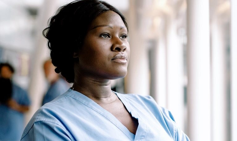 Contemplating female nurse with arms crossed looking through window in hospital