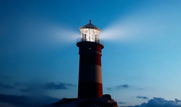 This image depicts a tall lighthouse with a prominent red and white striped pattern against a dark blue sky. The structure is situated on a dark, rocky foundation at the water's edge. The lighthouse is actively shining a bright, focused beam of light from its top lantern room.