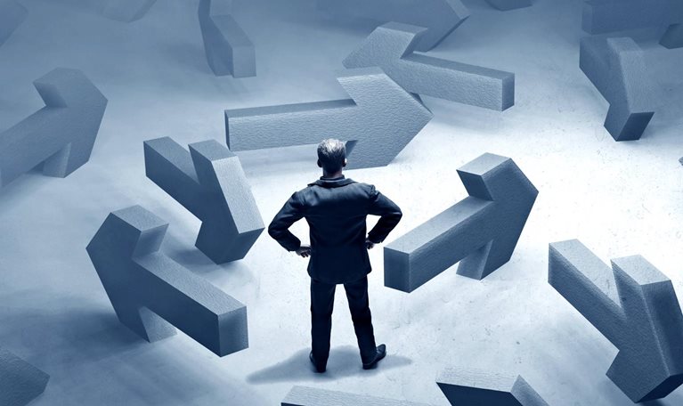 A multitude of large, concrete arrows pointing in different directions surround a businessman.