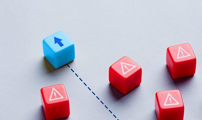 A blue cube, marked with an upward arrow, moves along a dotted path, navigating through a group of red cubes that are marked with warning symbols.