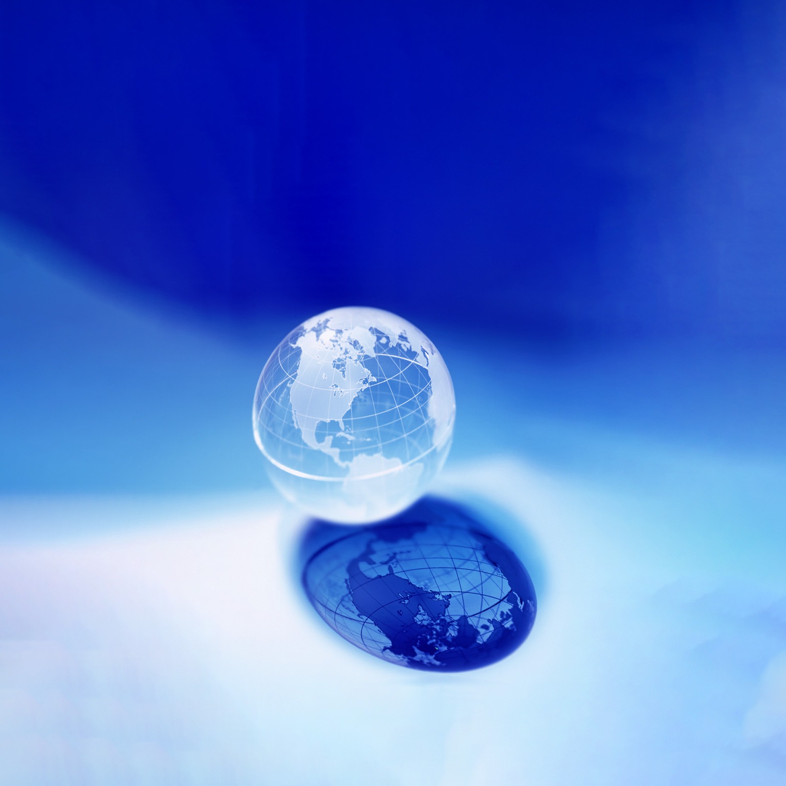 A translucent globe, with North and South America in focus, rests against a vibrant blue backdrop. Its reflection creates a darker, mirrored image below. 