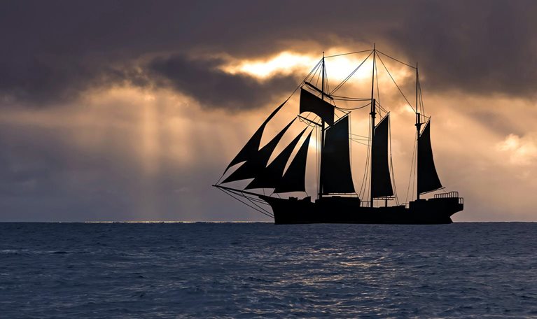 Image of a sailboat at sunset in a stormy sea.