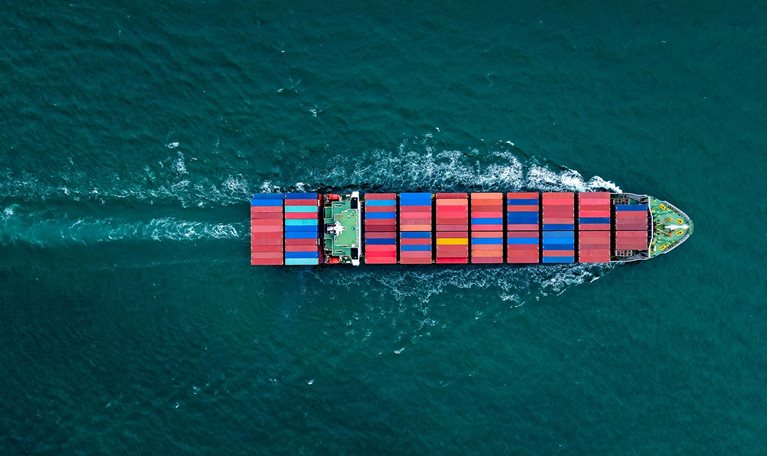 Overhead view of a large container ship sailing with many stacks of colorful containers visible on board