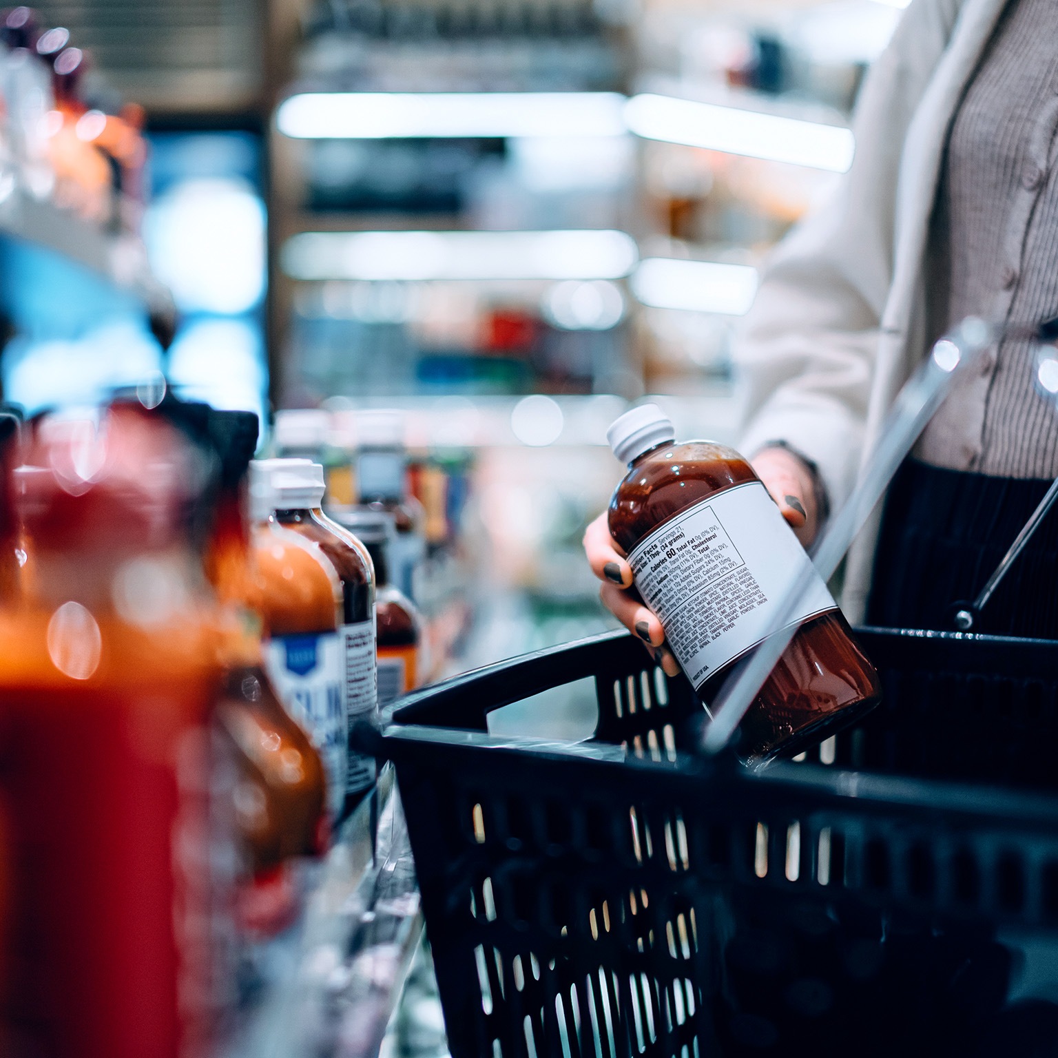 Close-up image of a woman putting a bottle into her shopping basket while shopping in a supermarket.