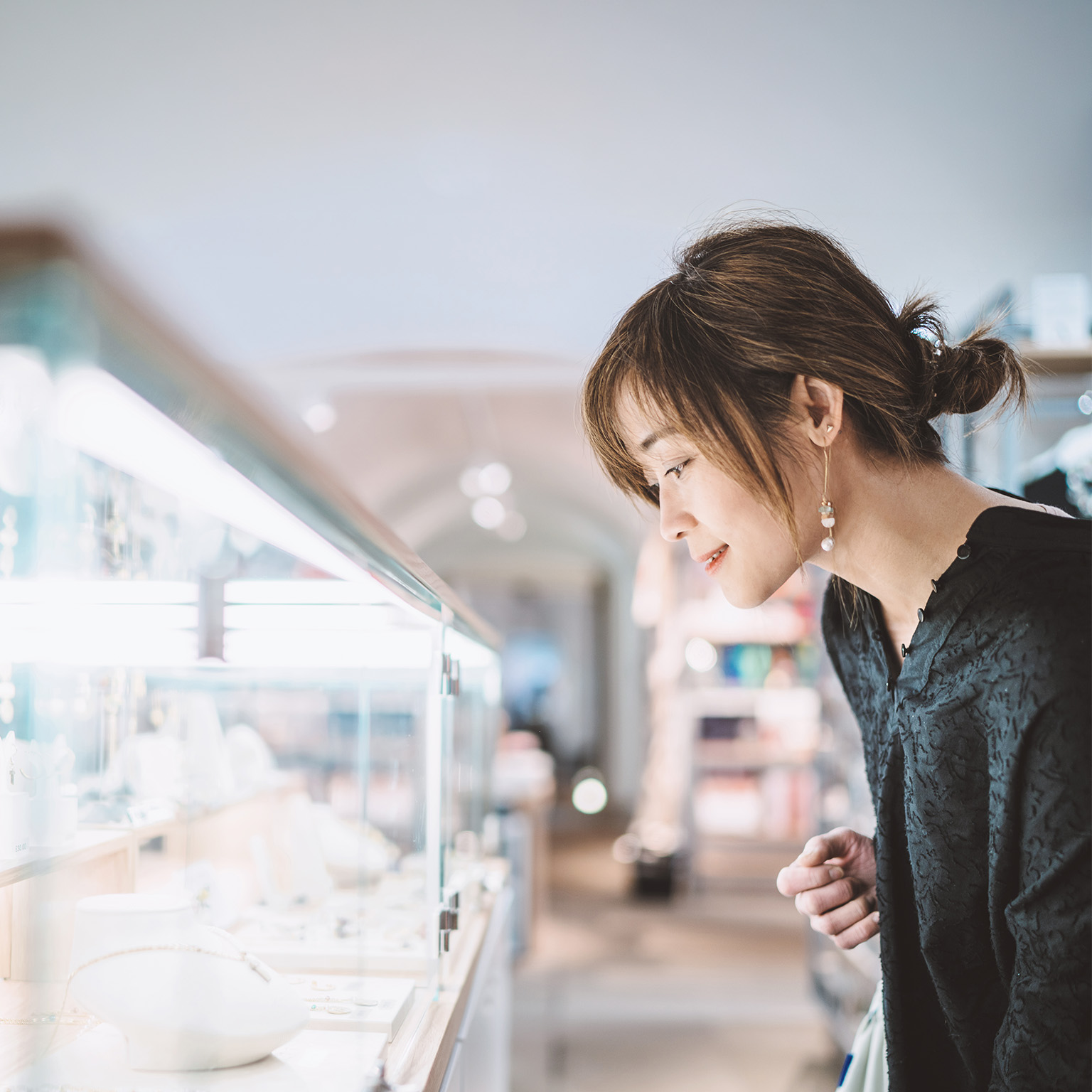 Young woman looking at jewelry through a glass display cabinet in a jewelry shop.