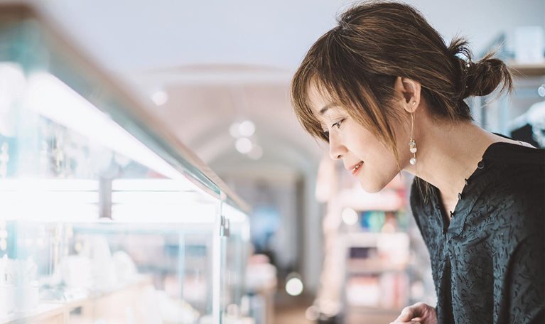 Young woman looking at jewelry through a glass display cabinet in a jewelry shop.