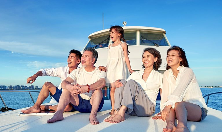 Image of an Chinese family cherishing the sunset while smiling and laughing, sitting on the front of a boat looking out to sea.