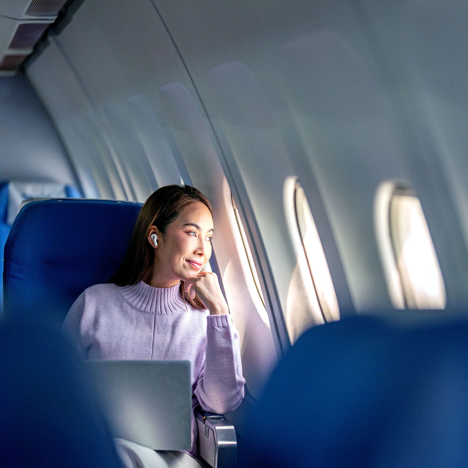 A woman passenger working mid-flight stops to gaze out her airplane window.