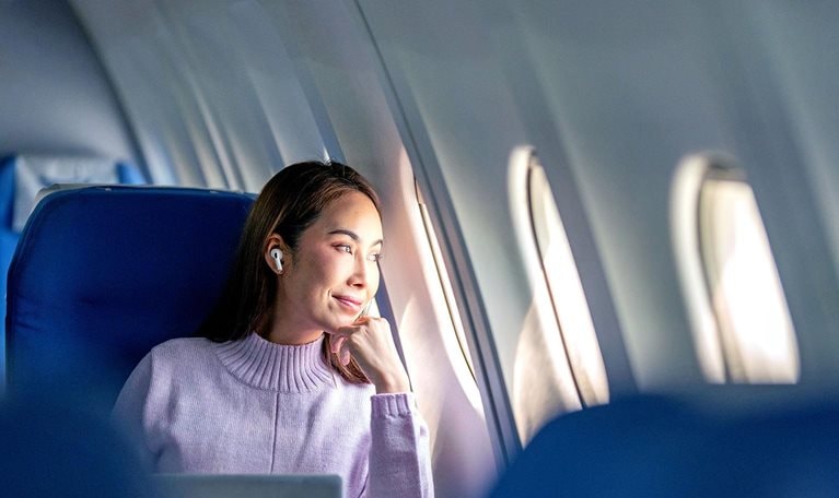 A woman passenger working mid-flight stops to gaze out her airplane window.