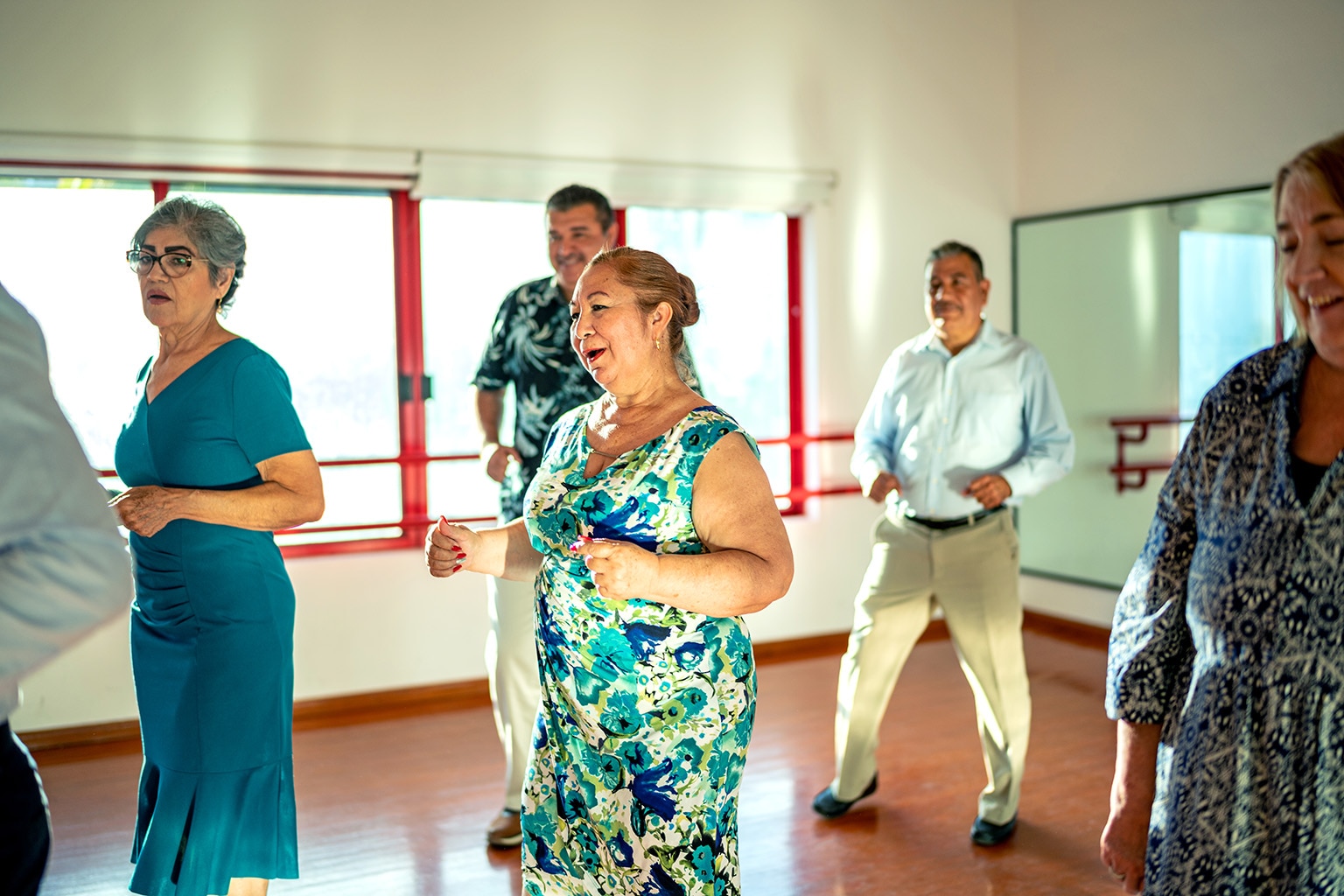 A group of smiling seniors participating in a dance class at a senior home.