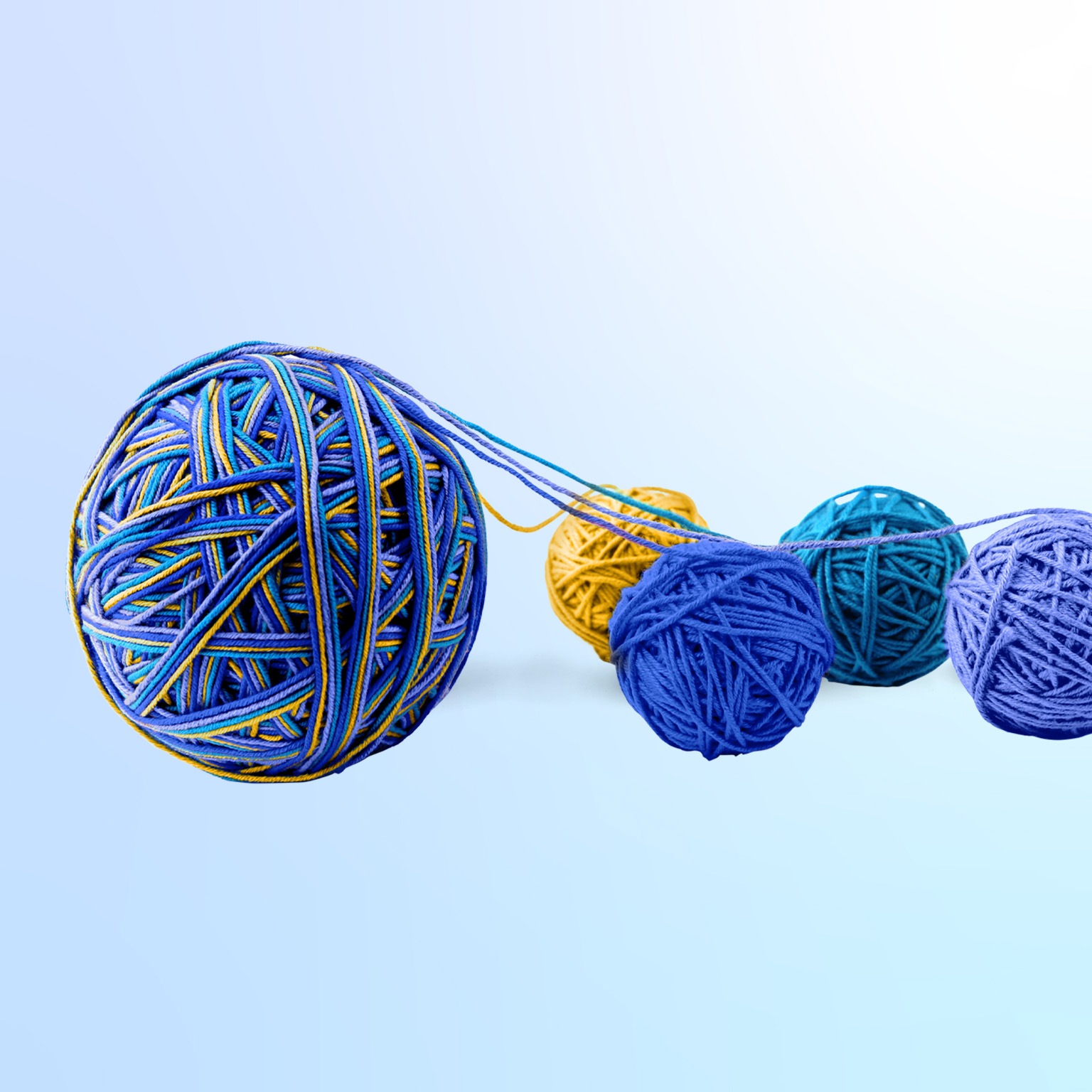 A large yarn ball composed of various hues, originating from four smaller yarn balls. The smaller balls come in diverse tones of blue, with one exception of yellow, and are positioned next to the larger ball.