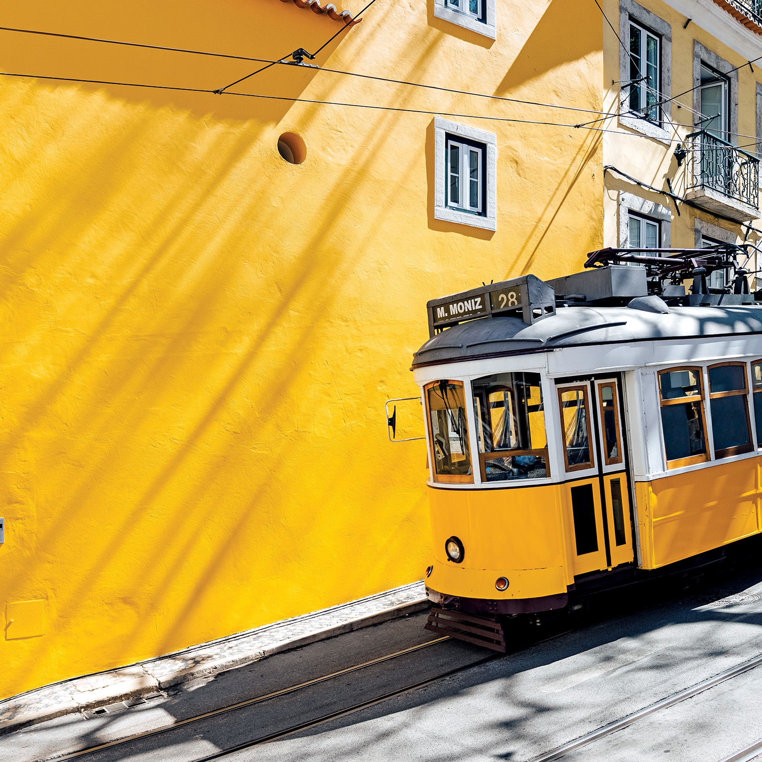 Yellow tram moving past yellow building in Lisbon, Portugal