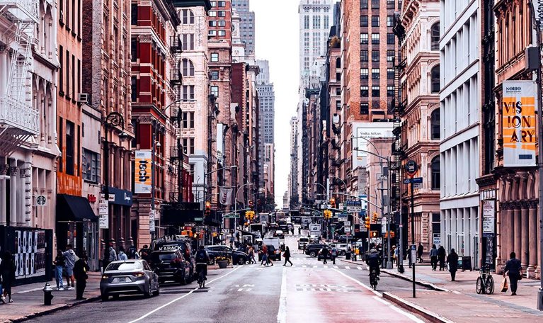 A bustling New York City street lined with historic buildings, shops, and pedestrians.