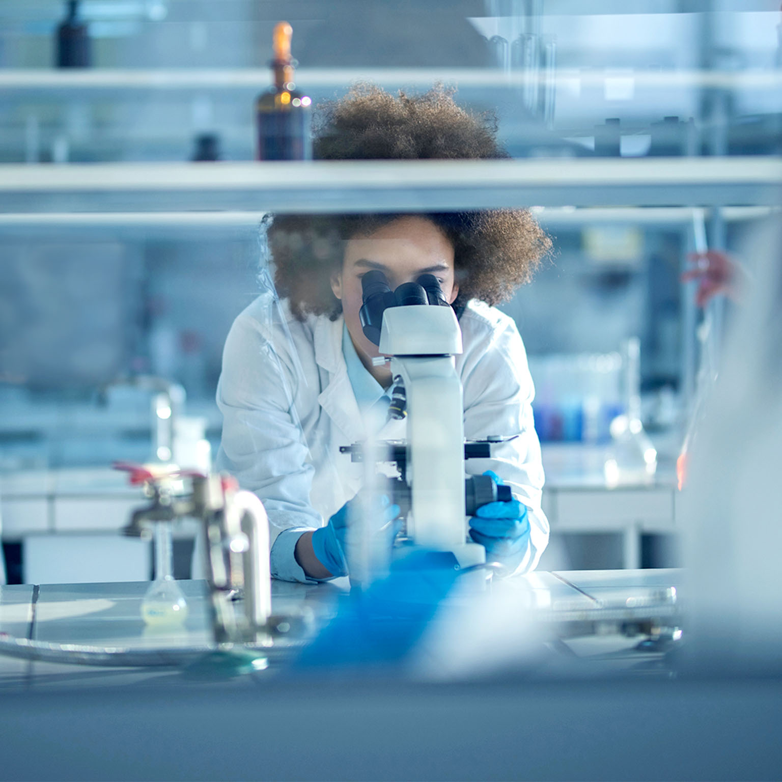 Young African American biochemist using microscope while working on scientific research in a laboratory. 