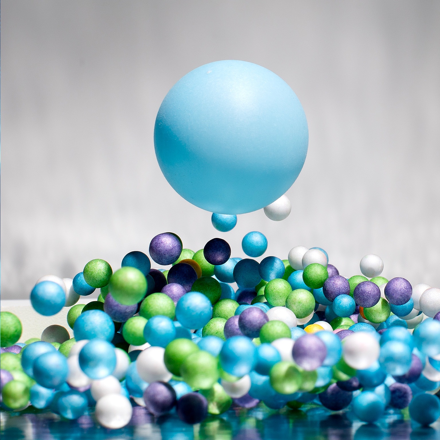 One large blue ball in mid air above many smaller blue, green, purple and white balls