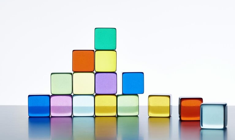 A pyramid made of vibrant transparent cubes against a white background. The pyramid is incomplete on the right side, and there are extra cubes lying next to it.