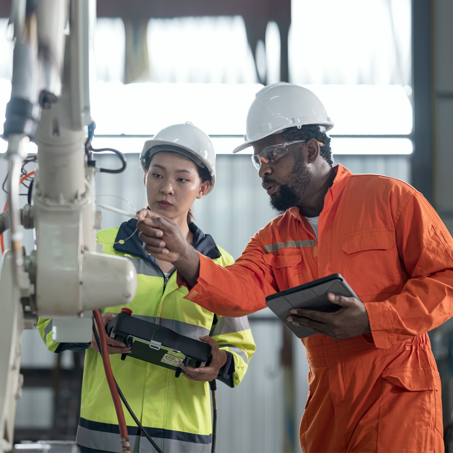 man and woman inspecting safety of robotic arm in factory