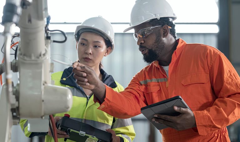 man and woman inspecting safety of robotic arm in factory