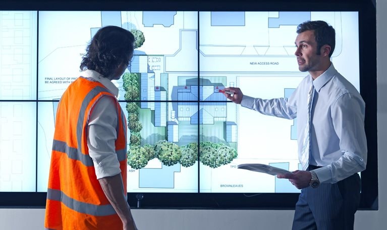 Construction worker and architect look at construction plans on digital screen