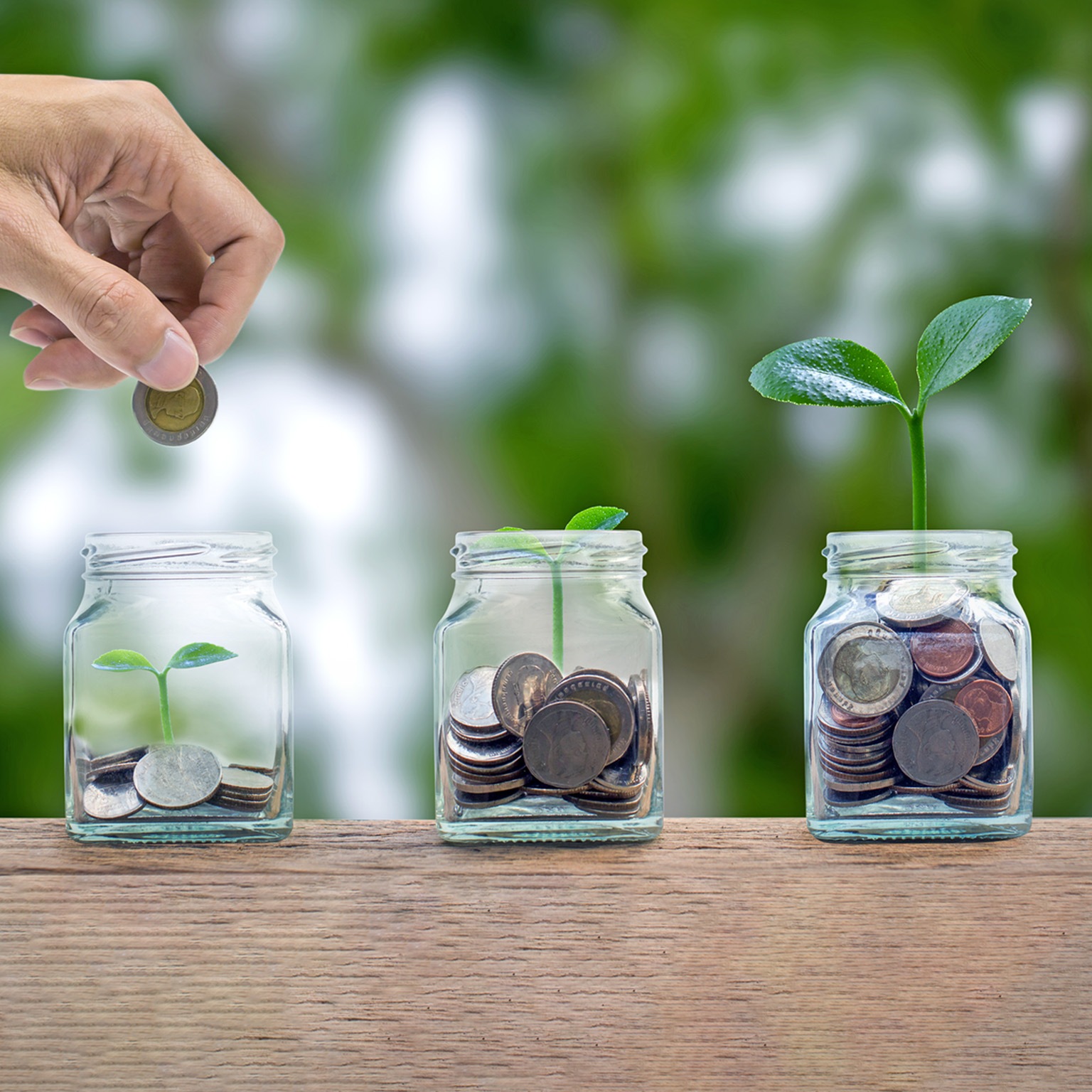 A hand putting a coin into a glass bottle containing coins