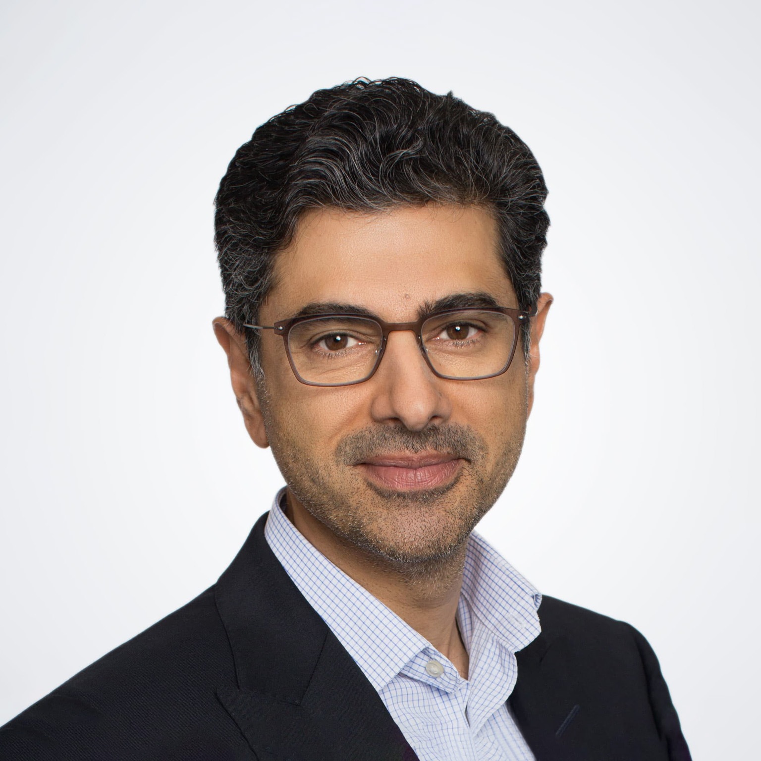 A photograph captures Alok Sama in a suit jacket and button down shirt, smiling gently against a white background.