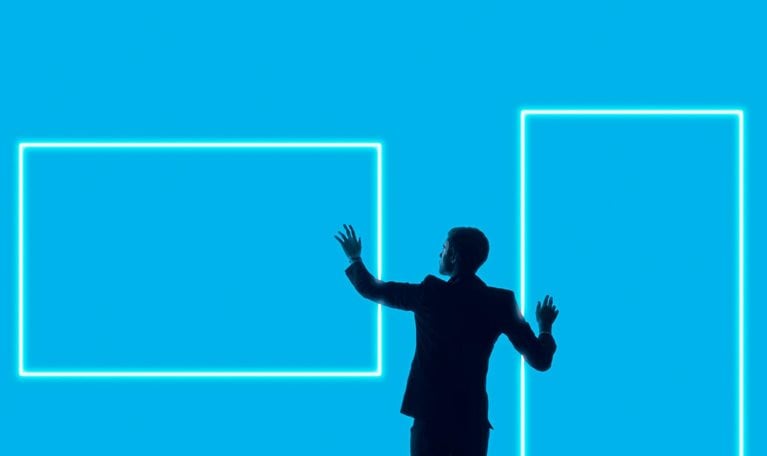 A silhouetted man in a suit stands against a bright blue background, reaching toward two glowing rectangular outlines that resemble digital screens or frames.