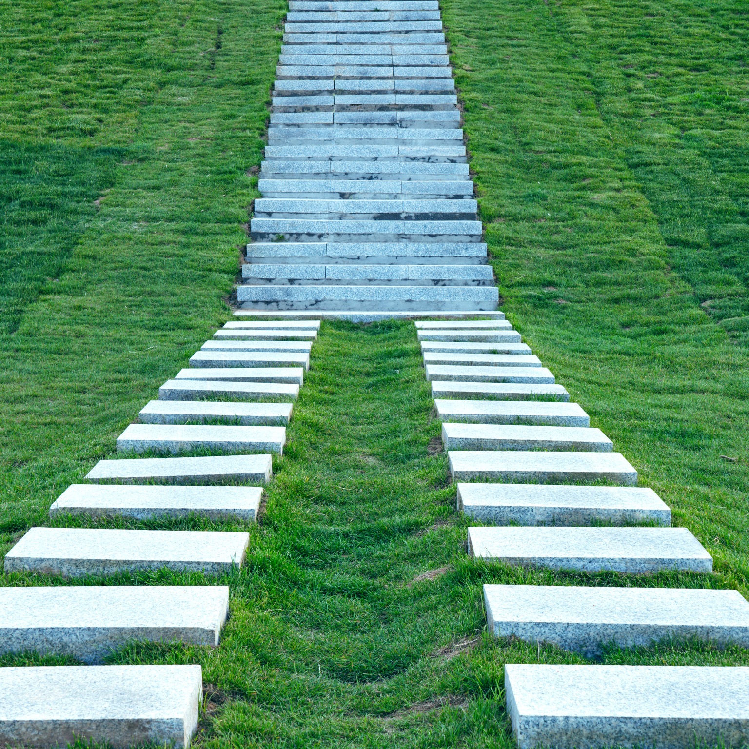 Two stone paths come together to create a staircase that leads up a grassy hill.
