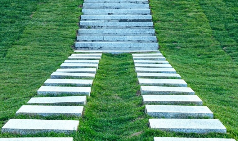 Two stone paths come together to create a staircase that leads up a grassy hill.