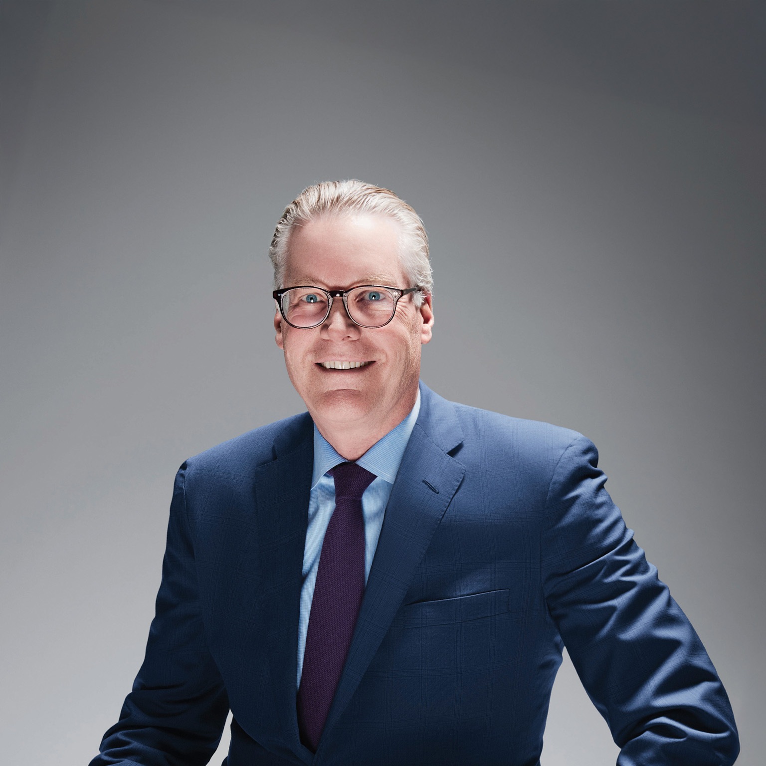 Ed Bastian, sporting a pair of glasses and dressed in a blue suit, light blue shirt, and a purple tie.