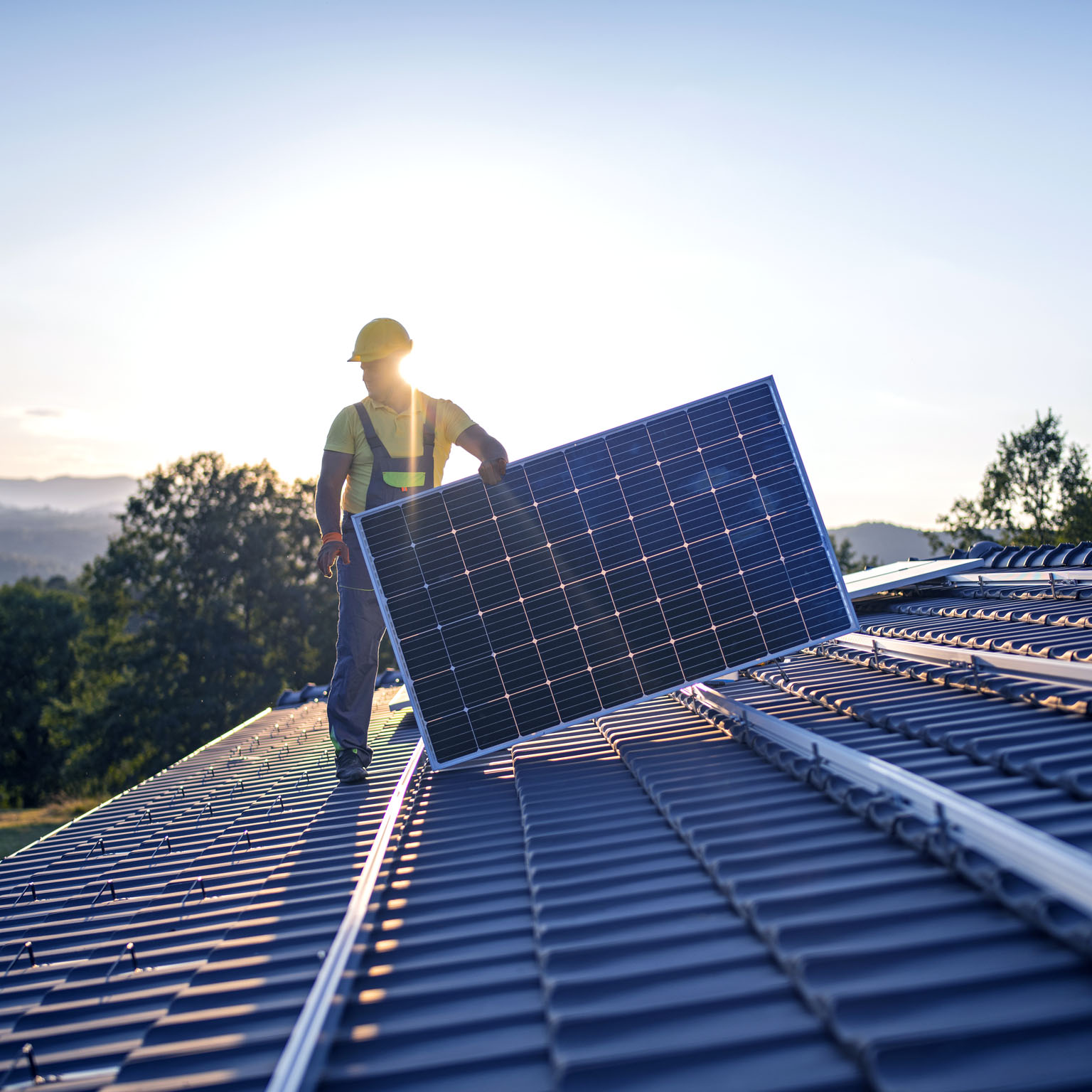 An image of a worker installing solar panels on the roof of a house.